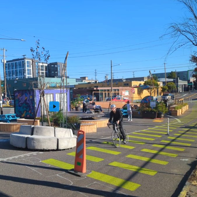 A cyclist rides through the pop-up plaza past planters and a painted crossing
